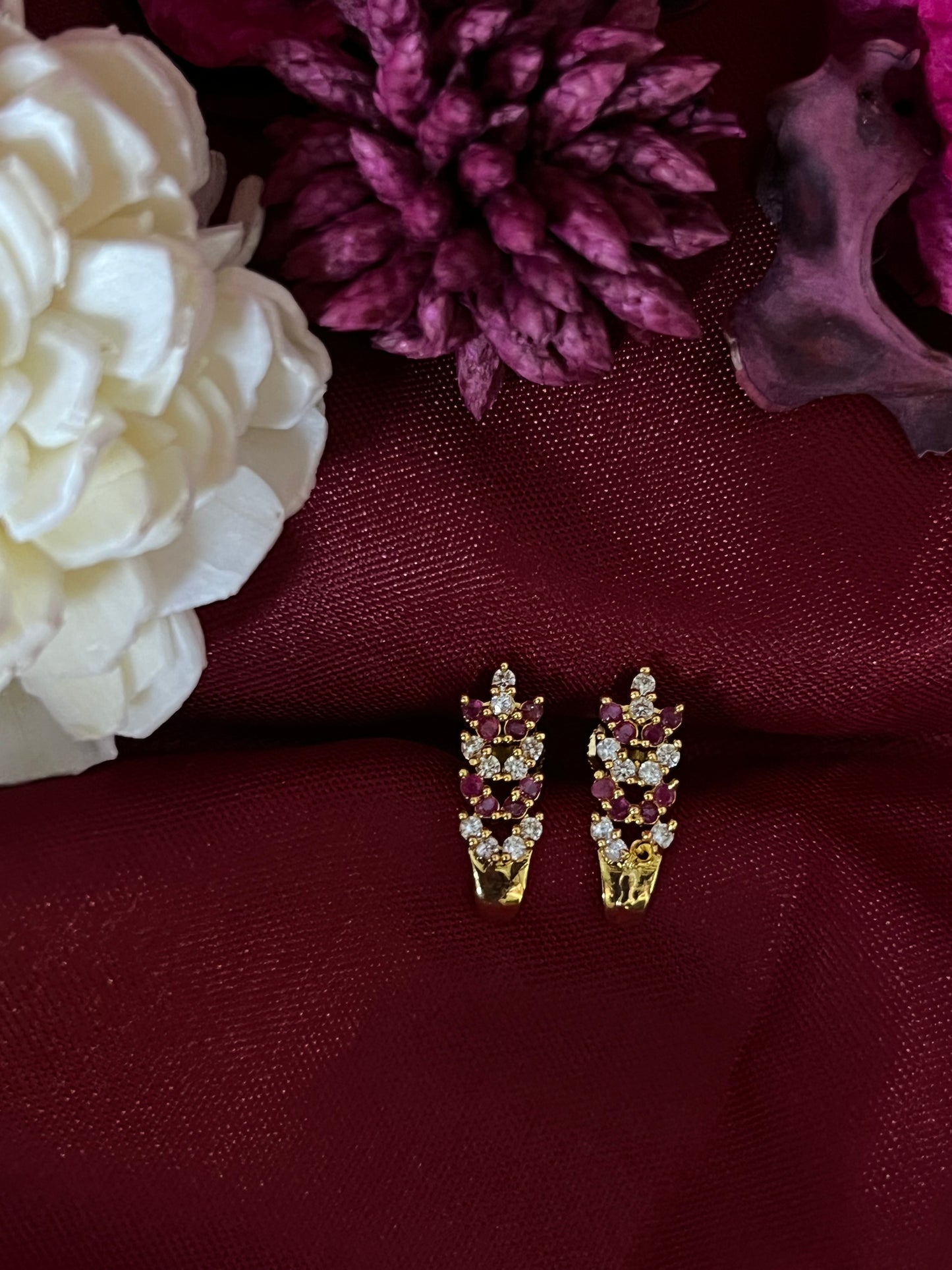Pair of gold and gemstone earrings on a burgundy fabric background with flowers.