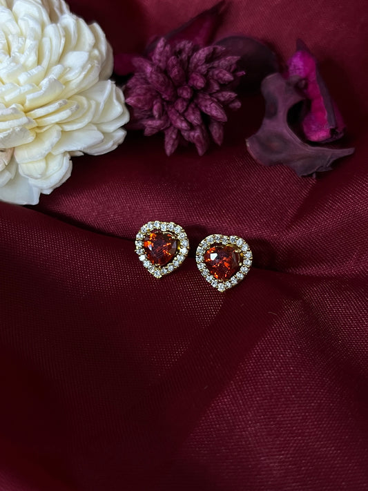 Heart-shaped earrings with red gemstones on a burgundy fabric background with flowers.