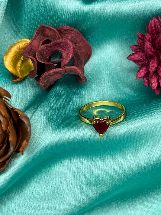 Gold ring with a red gemstone on a teal fabric background